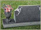 horizontal base slab with a vertical monument with face slanted with words engraved and a granite vase to the left of the vertical with flowers in it